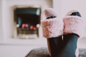 A person is wearing cozy socks and shoes and sitting next to a heating device  