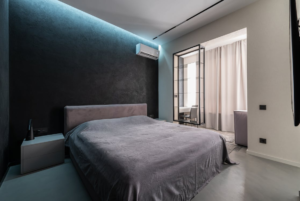 A spacious bedroom with a neatly made bed and an air conditioner installed on the wall.