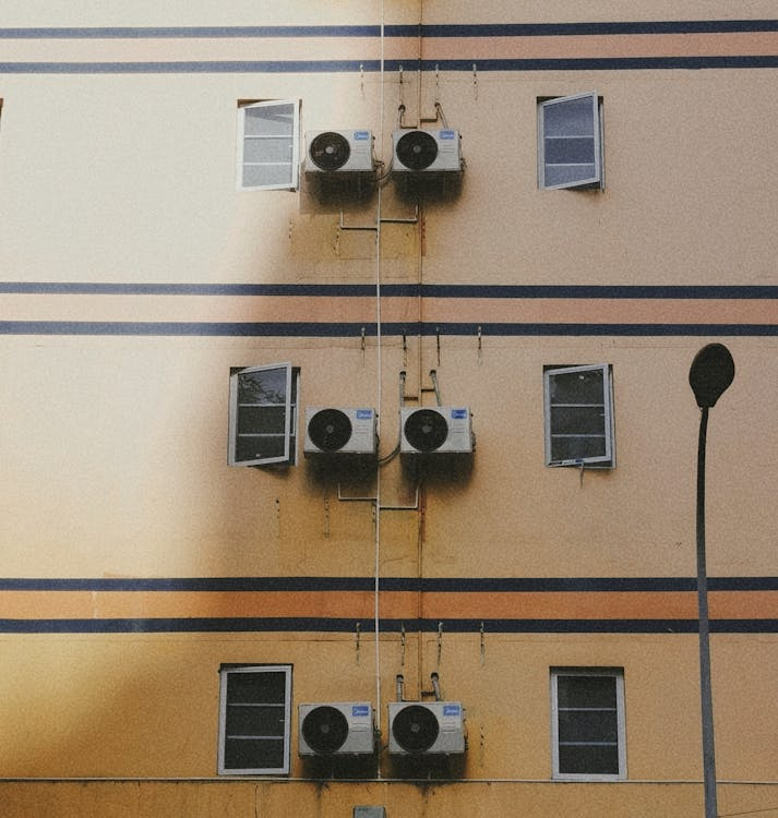 Multiple air conditioning systems mounted on a yellow wall.