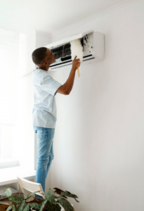 Man cleaning a wall-mounted air conditioner with a duster