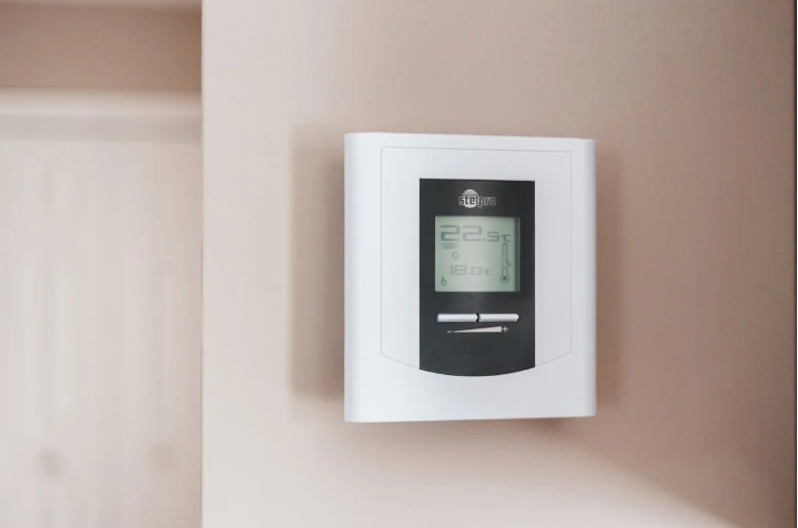A white digital thermostat mounted on a beige wall.