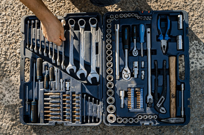 A hand reaching into an open black toolbox filled with various tools on the ground