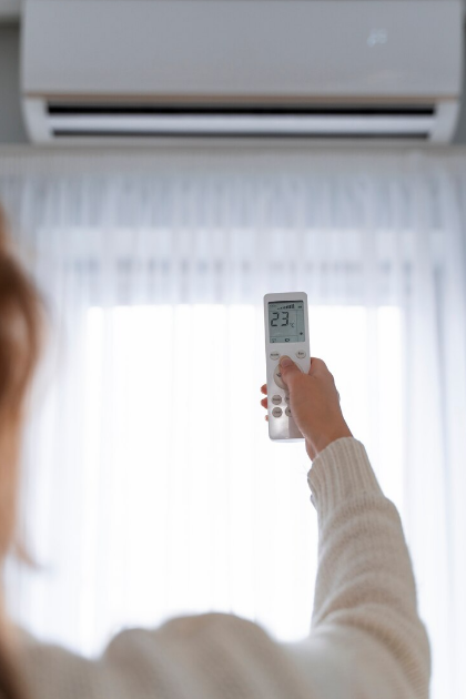 A person holds a remote control pointed at an air conditioning unit