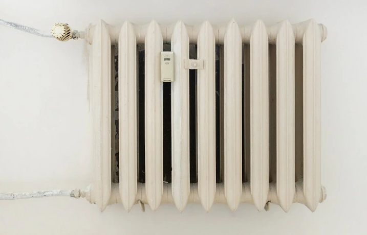 A white cast iron radiator with a digital thermostat attached, mounted on a white wall.