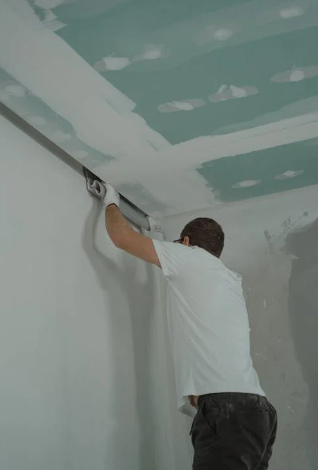 A construction worker applies joint compound to drywall seams on a wall and ceiling