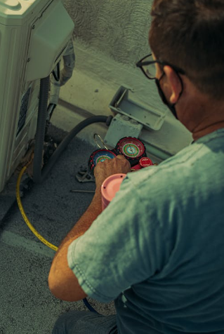 A technician working on an outdoor air conditioning unit with gauges and hoses